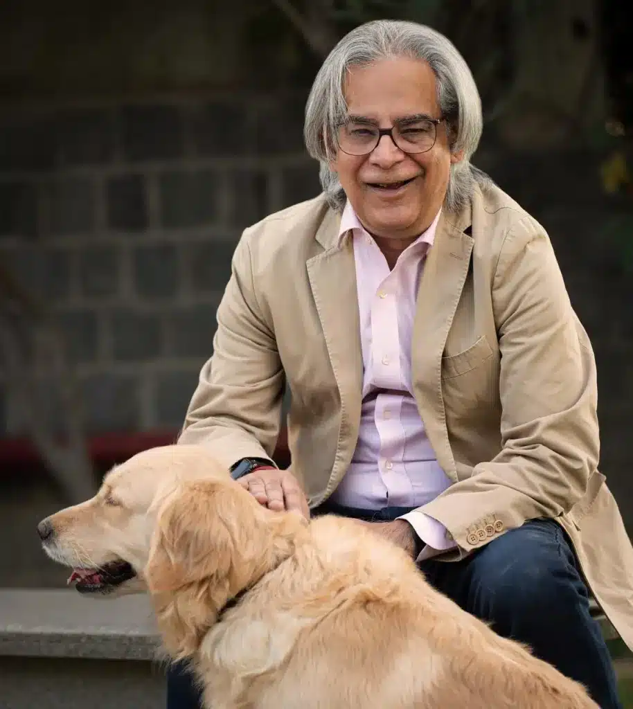 Sumer Datta A joyful man in a beige blazer, sitting with a golden retriever, symbolizing warmth and the journey "From Garage to Coma to Global: Sumer Datta’s Journey".